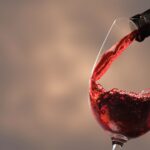 Pouring Red Wine Into Glass From Bottle Against Blurred Beige Background Closeup Space Text 150x150